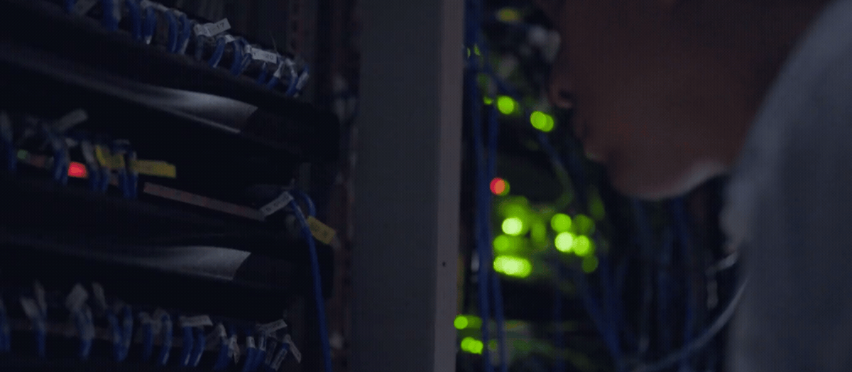 Technician in a long-sleeved button-down shirt plugs in a wire to a server in a server room within a micro data center.